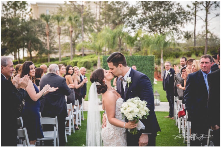 Cream and champagne Orlando wedding Omni Resort at Championsgate Brandon Kari Productions A Chair Affair hedgewood wall kiss at ceremony