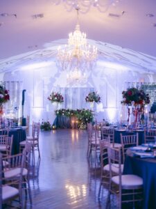 A wedding reception filled with blue linen covered tables and gold chairs inside the The Highland Manor.