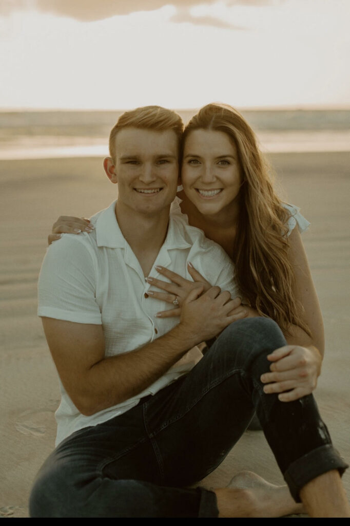 A couple sitting on the beach for engagement photos who won A Chair Affairs Monthly Wedding Rental for $500 off.