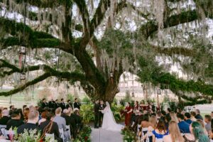 Highland Manor Wedding ceremony, the bride and groom pictured holding hands as guests look on.