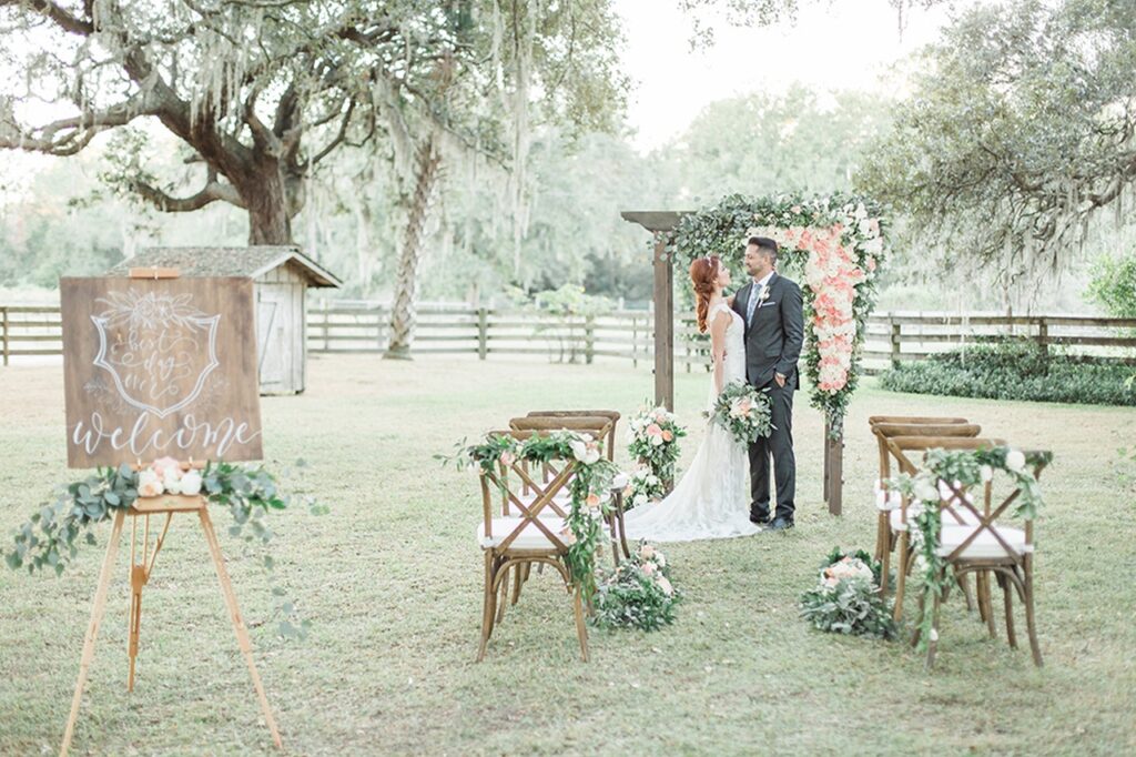 Isola Farms inspired wedding, bride and groom standing at the end of the aisle in front of wedding arch covered in flowers.
