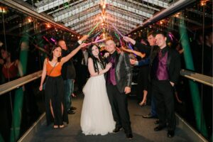 The bride and groom being sent off by guests with their glow sticks in the hallway with only windows.