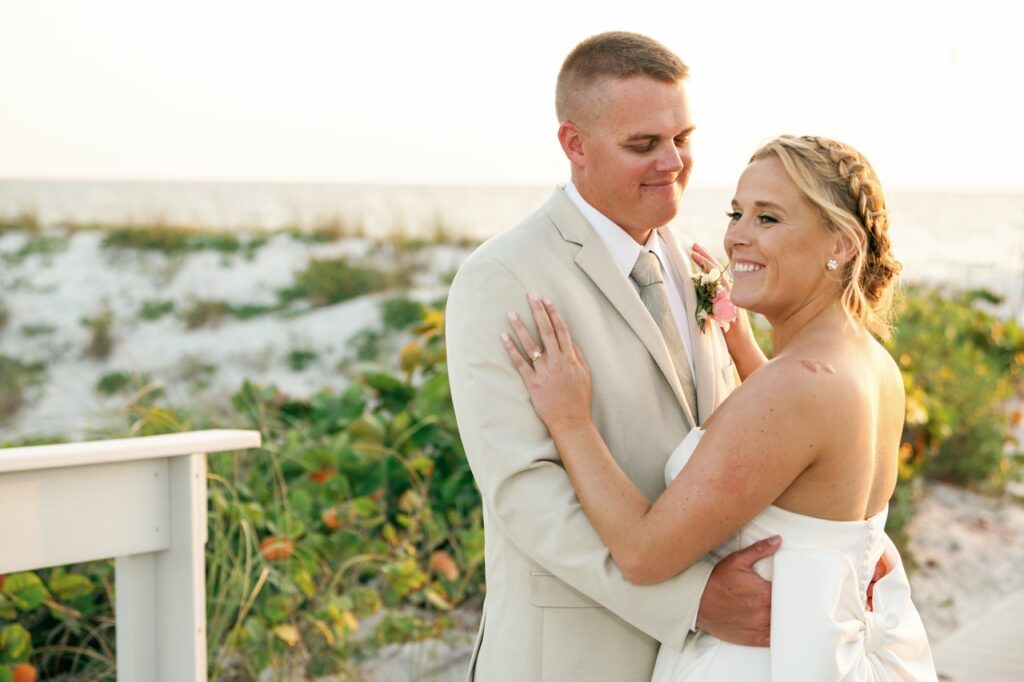 Bride and groom embracing with the sand and beach in the background with the sun setting