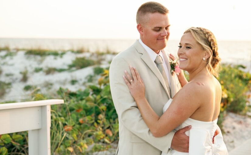 Bride and groom embracing with the sand and beach in the background with the sun setting