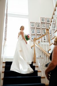 The bride captured in her wedding gown while holding her bouquet. She's pictured on the stairs with her head looking over her shoulder, while displaying the back of her gown