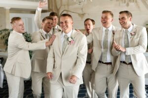 The grooms and his groomsmen in their tan suits standing around sharing laughs and smiling before wedding ceremony