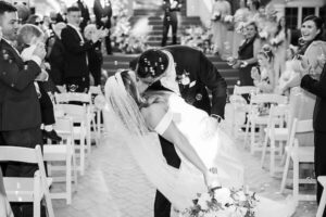 The groom dipping the bride while exiting the ceremony surrounded by family and friends all while bubbles are going off around them