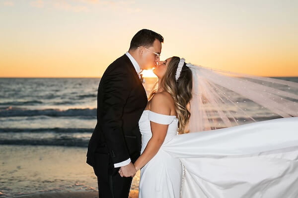 Bride and groom on St. Pete beach standing on the beach in front of the water and directly in front of the sunset sharing a kiss