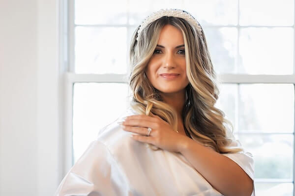 The bride captured in a photo before the ceremony in her wedding robe. Her hair is down and curled and she's sporting a pearl white headband