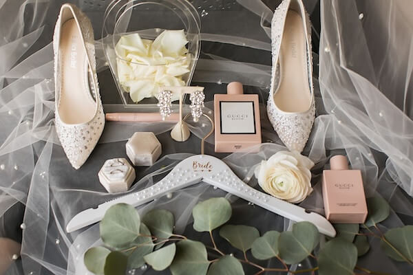 The wedding shoes, wedding jewelry, rings, perfume and hanger placed on top of wedding veil and captured in a picture