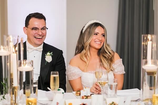 The bride and groom during the reception sitting at their wedding table laughing and smiling