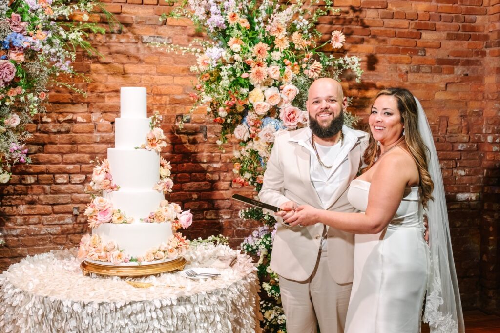 The bride and groom at the Armature Works reception standing next to the cake about to cut into it