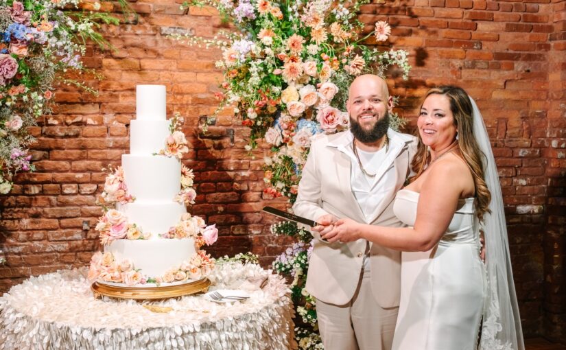 The bride and groom at the Armature Works reception standing next to the cake about to cut into it