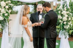 The couple standing in front of the officiant during the wedding ceremony and exchanging rings with one another