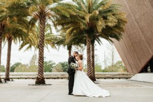 The bride in groom in their wedding attire captured in a photo outside the Winter Park Events center and in front of palm trees