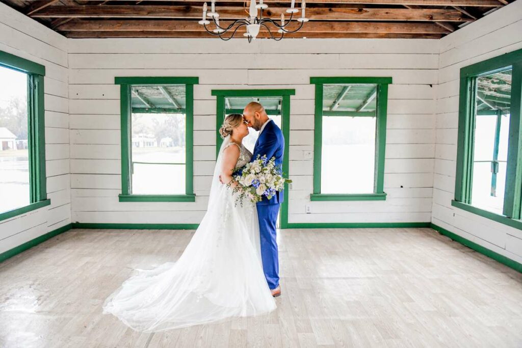 The bride and groom standing in a room with their wedding attire on. under a chandelier while embracing each other