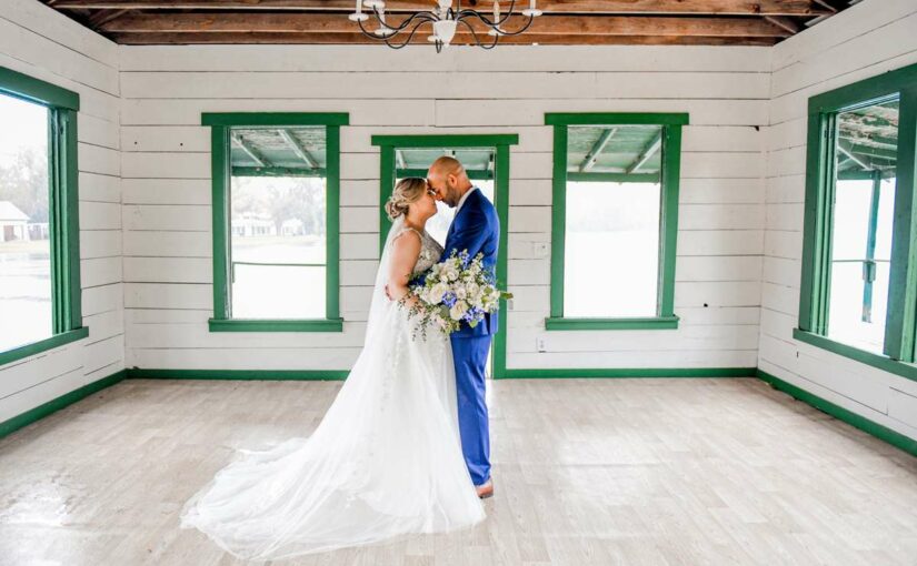 The bride and groom standing in a room with their wedding attire on. under a chandelier while embracing each other