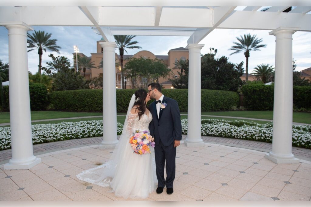 The bride and groom standing outside the Ritz-Carlton sharing kiss with the venue in the background while they're dressed in their attire