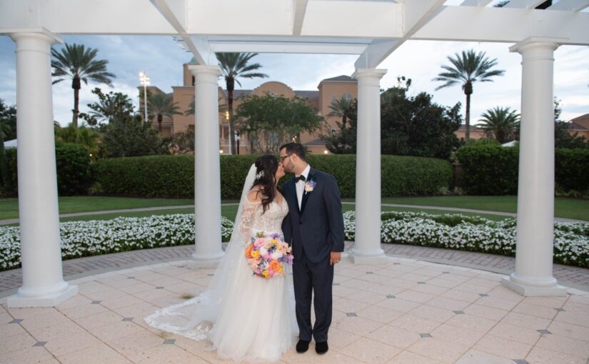 The bride and groom standing outside the Ritz-Carlton sharing kiss with the venue in the background while they're dressed in their attire