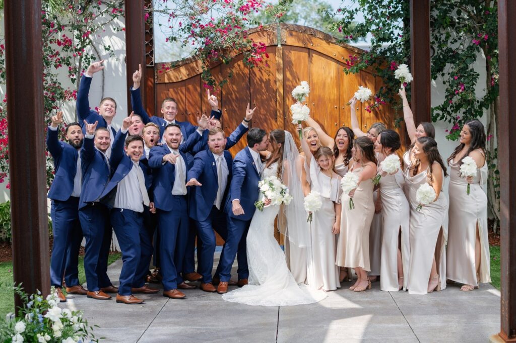 The wedding party outside The Venue 650 standing in a line in their wedding attire cheering on the bride and groom as they share a kiss at the center of the picture