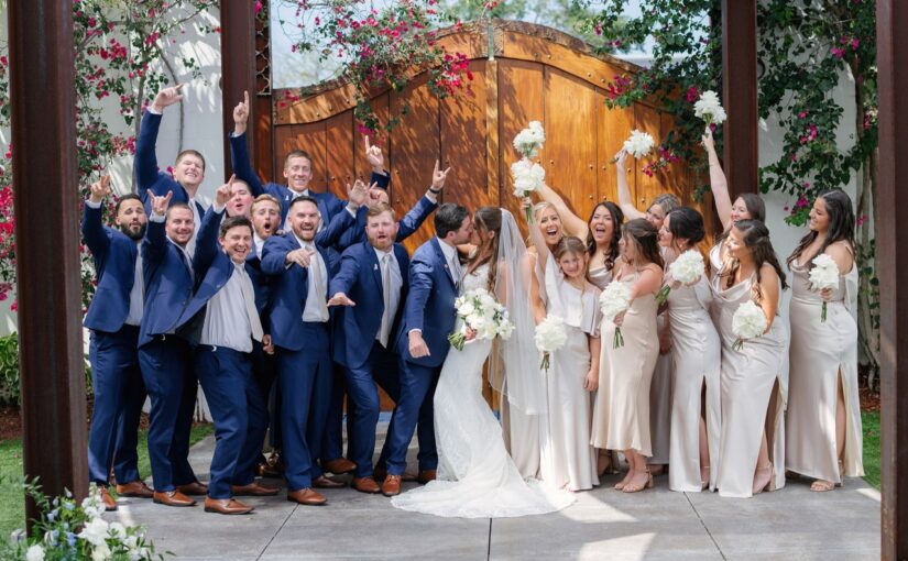 The wedding party outside The Venue 650 standing in a line in their wedding attire cheering on the bride and groom as they share a kiss at the center of the picture