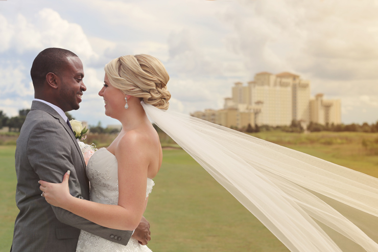 The bride and groom embracing with the Omni Champions Gate in the background and the brides veil blowing in the wind