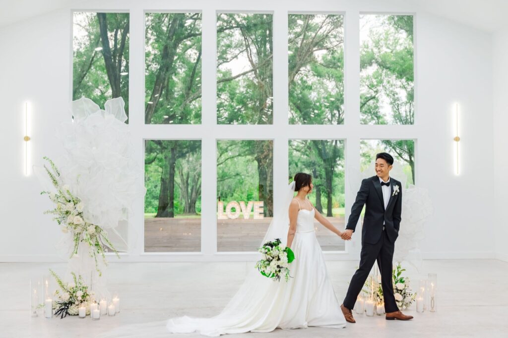 A photo of the bride and groom holding hands and walking in front of the floor to ceiling windows at the Whitewood Ranch