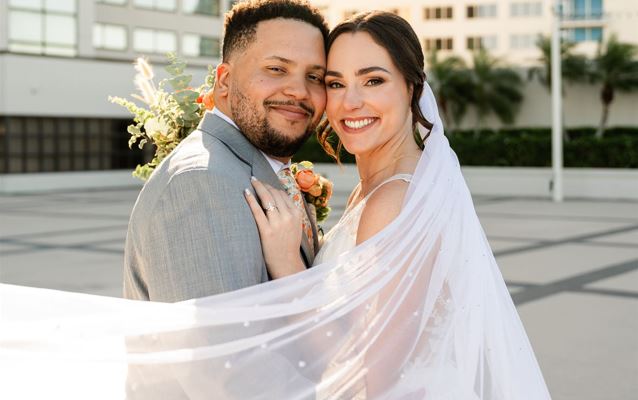 April Monthly Wedding Winner, Manny and Carley in wedding attire outdoors with their heads together as they pose for a picture