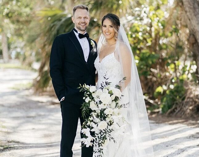 May Monthly Wedding Winners Sara and Kyle pictured in their wedding attire standing outside with greenery in the background