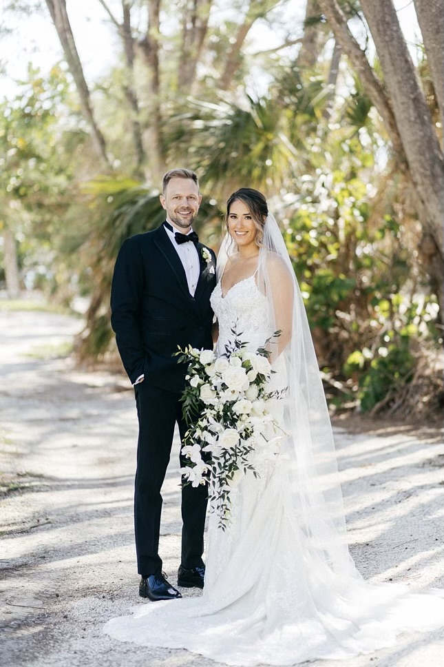 May Monthly Wedding Winners Sara and Kyle pictured in their wedding attire standing outside with greenery in the background
