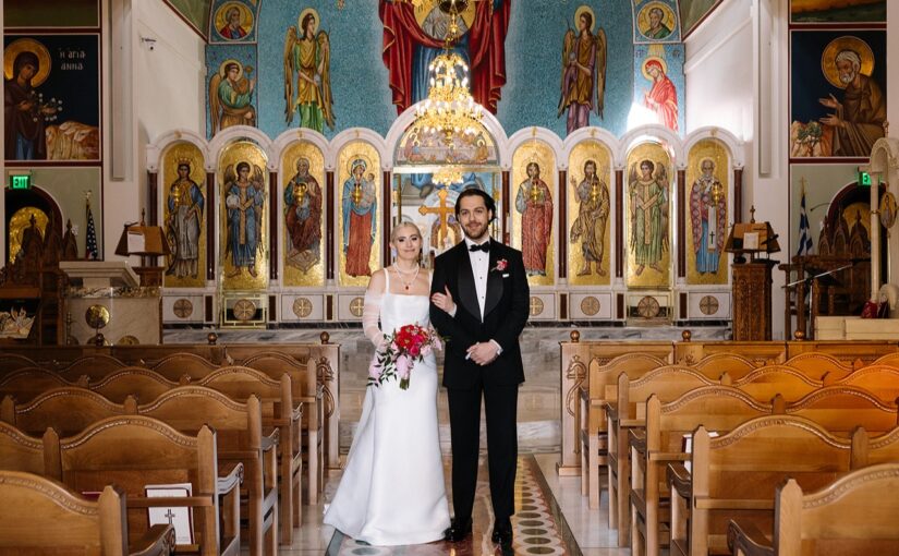 Kali and Zach Doyle on their wedding day May 25, 2024. Dressed in their wedding attire standing in the aisle at the Holy Trinity Orthodox Church