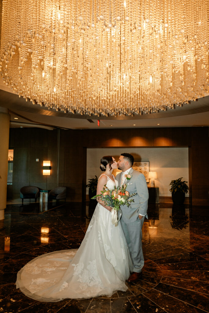 Bride and Groom kissing under gold chandelier at Hyatt Regency Orlando. Wedding Rentals Orlando.