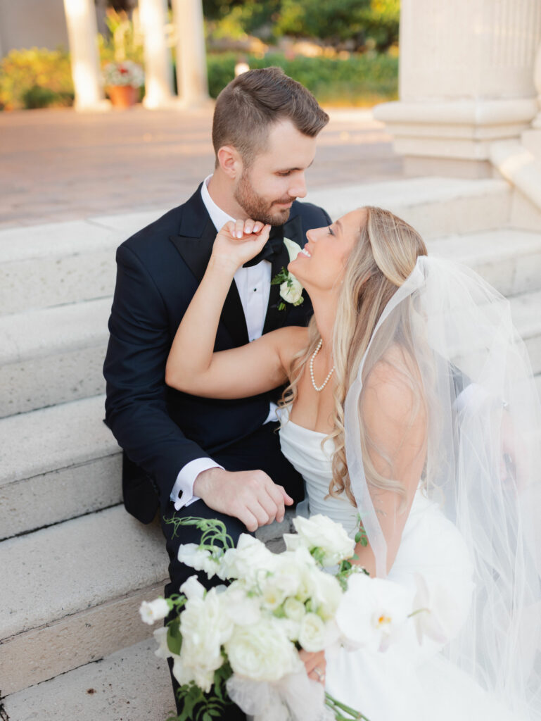 Bride gazing at groom on steps. Orlando Wedding Rentals. Navy Octo Chargers from A Chair Affair