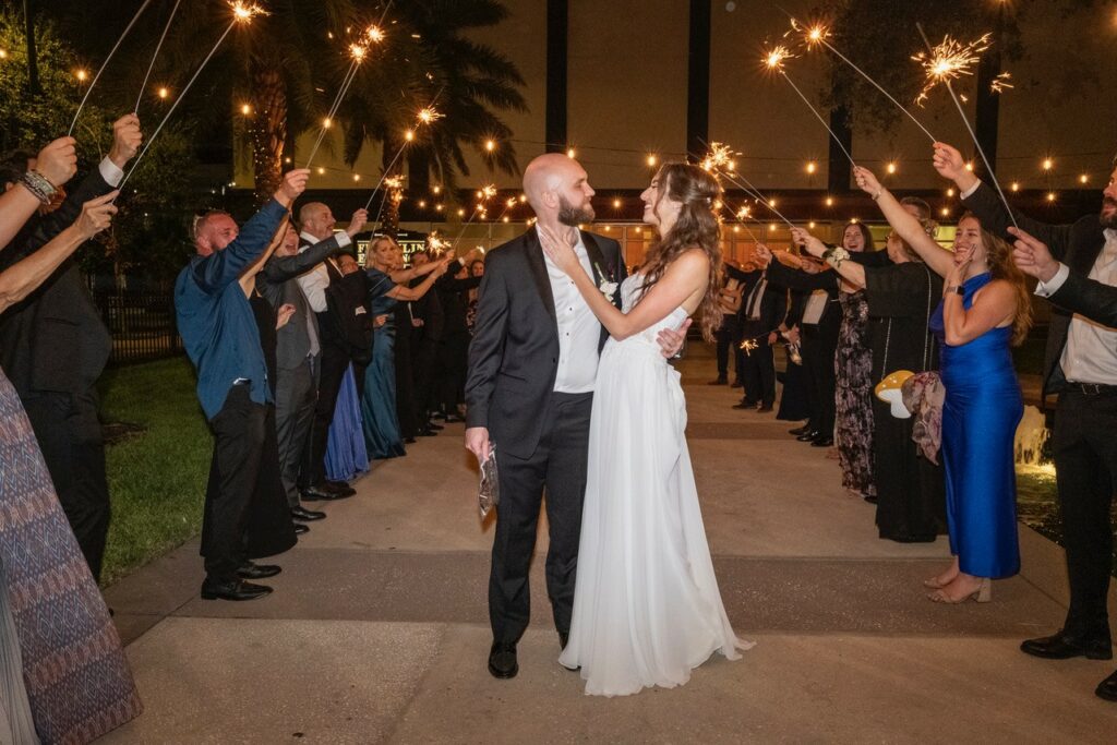 Bride and Groom exiting reception with chargers, linen and flatware provided by A Chair Affair. Central Florida Wedding Rentals. Orlando Wedding Rentals. Tampa Wedding Rentals. Gilded Glamour: A Luxurious Purple & Gold Tampa Wedding at The Vault