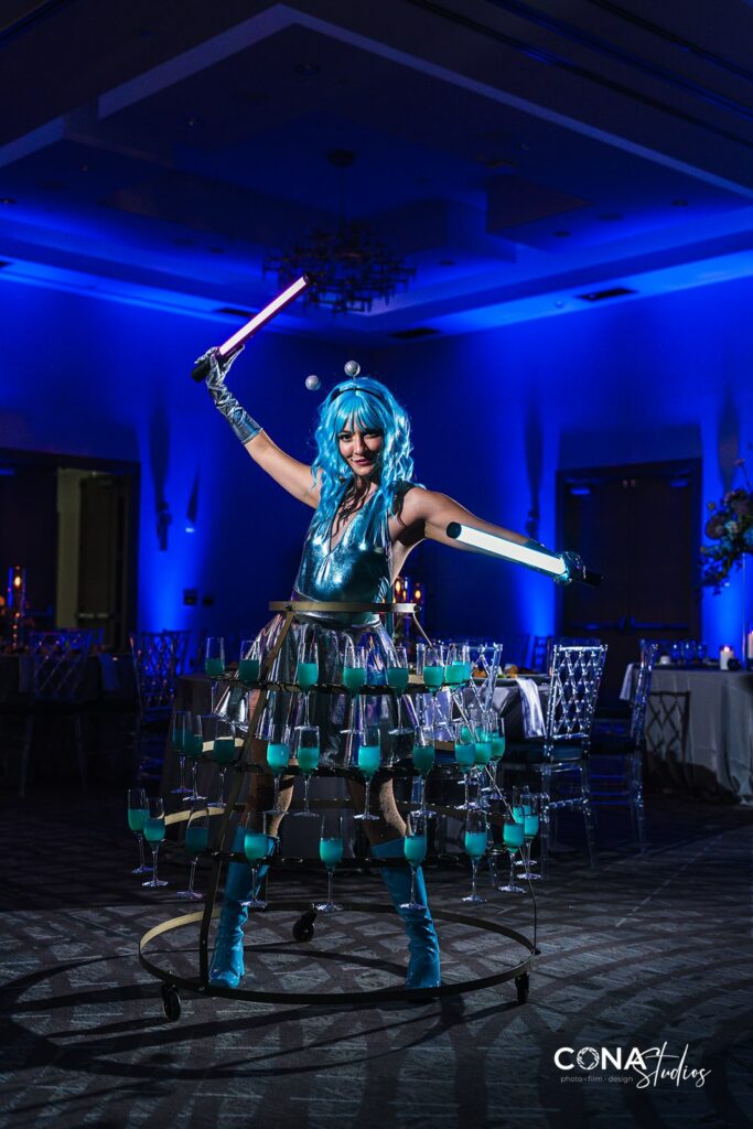 Martian entertainer with drink skirt in blue lighting. Art Deco Bar, Silver Glitter Spiral Glass Chargers, Clear Wysteria Chairs and Cobalt Blue Goblets provided by A Chair Affair at the CFWA and NACE Orlando Annual Meeting at The Celeste Hotel.