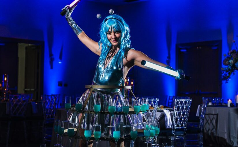 Martian entertainer with drink skirt in blue lighting. Art Deco Bar, Silver Glitter Spiral Glass Chargers, Clear Wysteria Chairs and Cobalt Blue Goblets provided by A Chair Affair at the CFWA and NACE Orlando Annual Meeting at The Celeste Hotel.